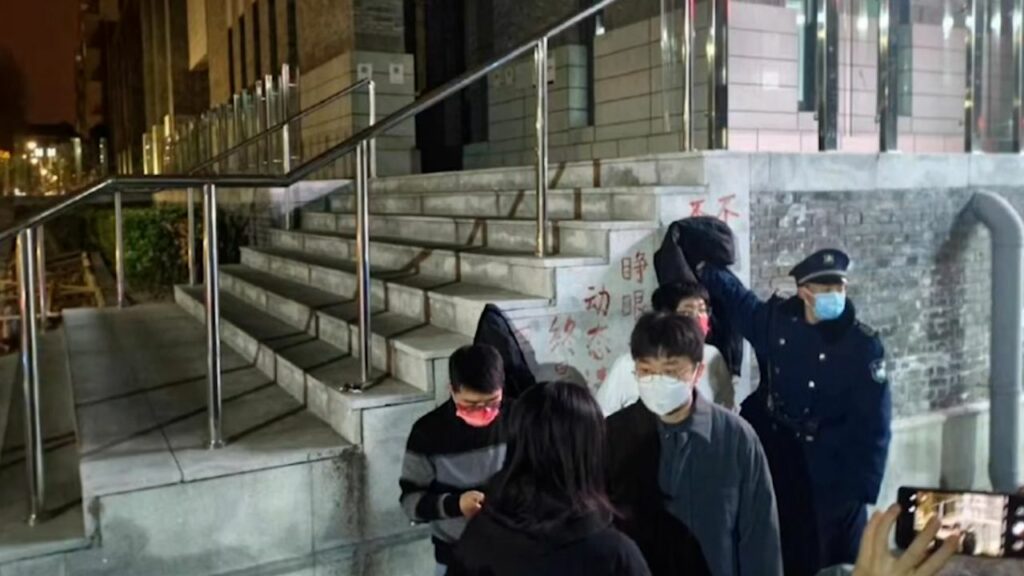 حارس أمن يغطي شعار احتجاجي ضد صفر كوفيد في حرم جامعة بكين